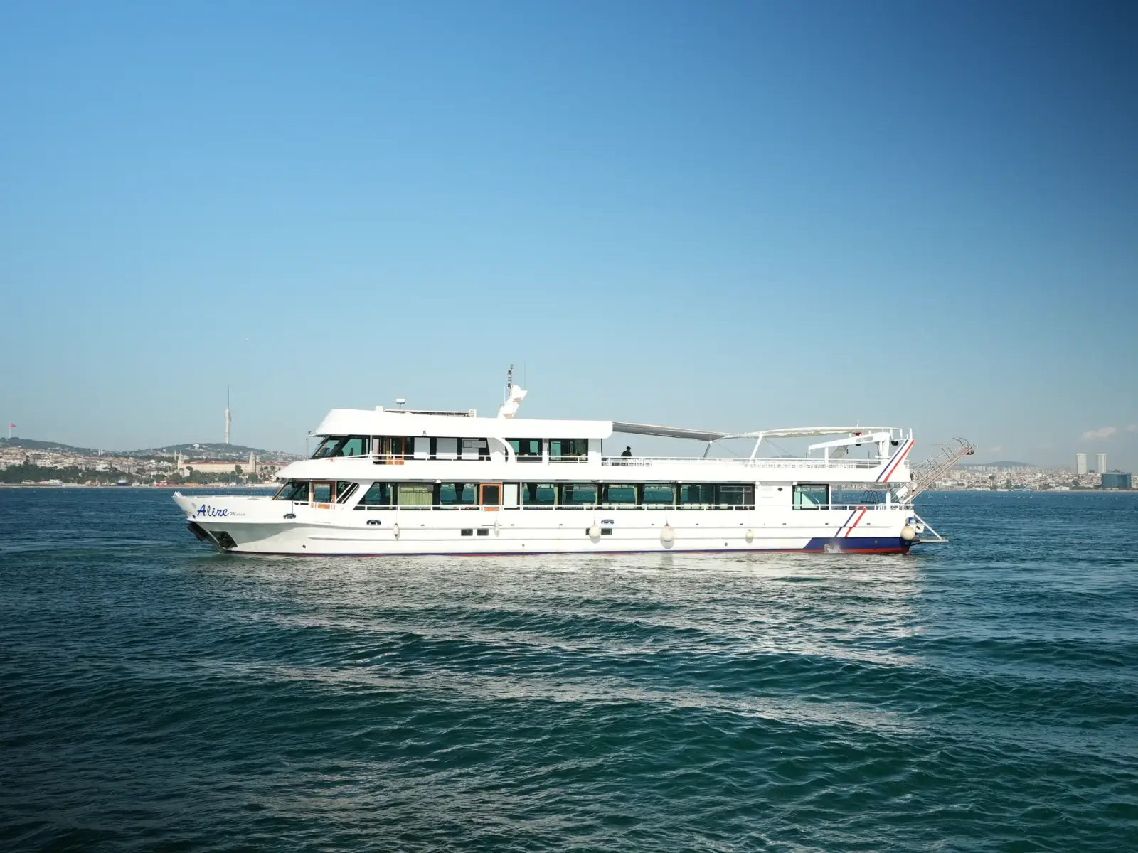 Ein weißes zweistöckiges Ausflugsschiff auf dem blauen Wasser des Bosporus