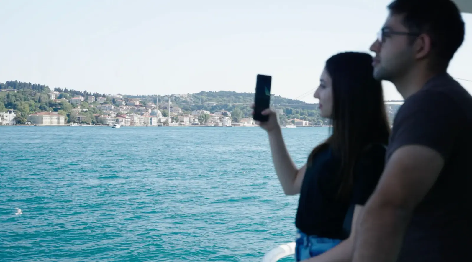 Zwei Gäste an der Reling filmen das Ufer mit dem Handy